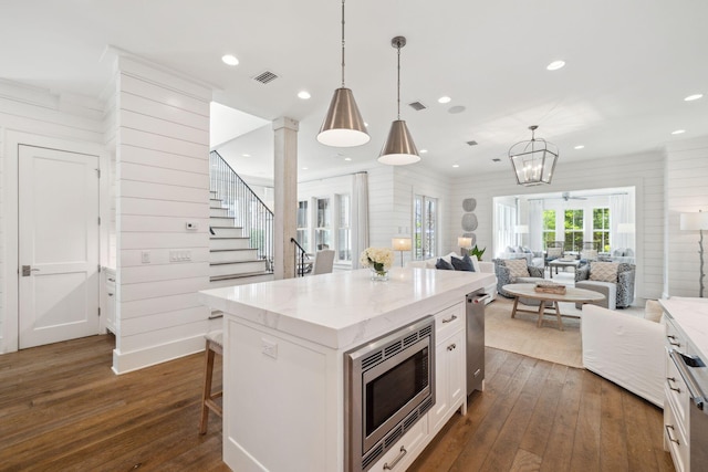17 Compass Point Way, Watersound, FL 32461 - kitchen with stainless steel microwave, dark wood-style flooring, open floor plan, white cabinetry, and light stone countertops