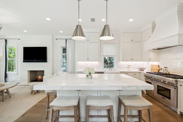 17 Compass Point Way, Watersound, FL 32461 - kitchen featuring range with two ovens, premium range hood, open floor plan, a center island, and a fireplace