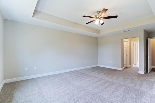 carpeted spare room with ceiling fan, baseboards, and a tray ceiling