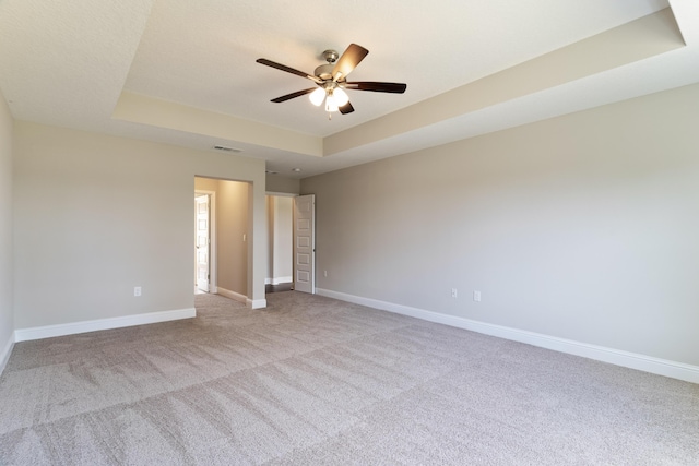 unfurnished room featuring a raised ceiling, carpet, baseboards, and a ceiling fan