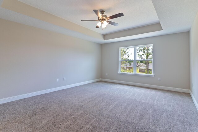 carpeted spare room featuring baseboards, a ceiling fan, and a raised ceiling