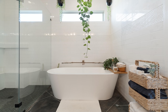 bathroom with plenty of natural light, a shower stall, a soaking tub, tile walls, and tile patterned floors