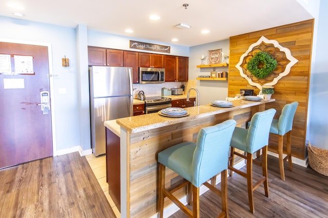 kitchen with appliances with stainless steel finishes, a peninsula, a breakfast bar, light wood-type flooring, and light stone counters