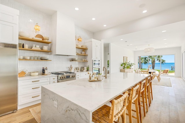 1341 Driftwood Point Rd, Santa Rosa Beach, FL 32459 - kitchen with open shelves, high end appliances, light wood-style flooring, white cabinetry, and a spacious island