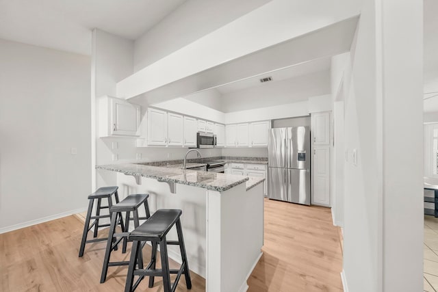 149 Kel Wen Cir, Destin, FL 32541 - kitchen featuring appliances with stainless steel finishes, a peninsula, light stone countertops, a kitchen breakfast bar, and white cabinets