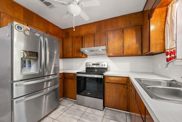 205 Florence Dr, Defuniak Springs, FL 32433 - kitchen with stainless steel appliances, under cabinet range hood, a sink, brown cabinets, and a textured ceiling
