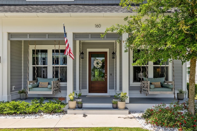 view of exterior entry with a shingled roof and covered porch