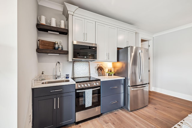 kitchen featuring stainless steel appliances, open shelves, a sink, light wood-style floors, and light countertops