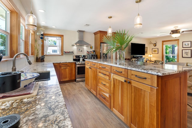 kitchen featuring wall chimney exhaust hood, light wood-type flooring, light stone counters, a sink, and brown cabinets
