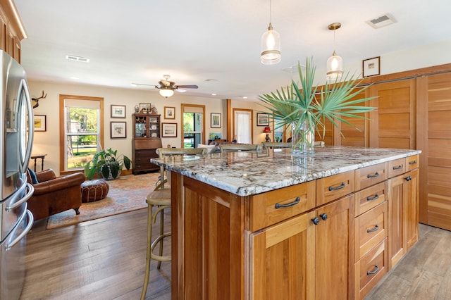 kitchen featuring stainless steel refrigerator with ice dispenser, open floor plan, a breakfast bar, light wood-style floors, and recessed lighting