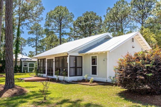 back of house with a sunroom, a lawn, an outbuilding, metal roof, and a storage unit