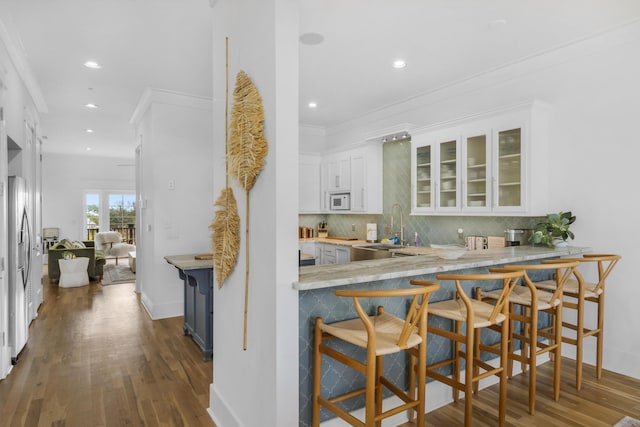 kitchen featuring white microwave, a sink, dark wood-type flooring, crown molding, and backsplash