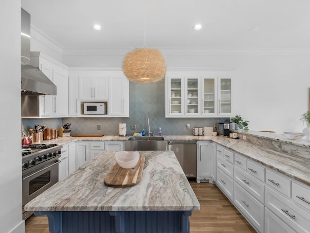 kitchen with appliances with stainless steel finishes, a sink, wall chimney exhaust hood, crown molding, and white cabinetry