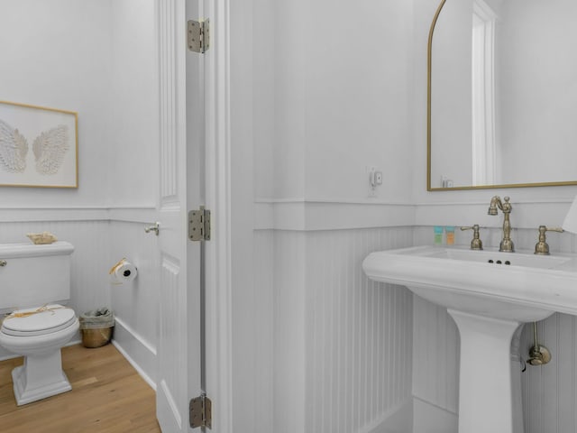 bathroom featuring toilet, wood finished floors, wainscoting, and a sink