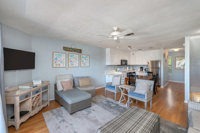living room with a ceiling fan, light wood-style floors, baseboards, and a textured ceiling
