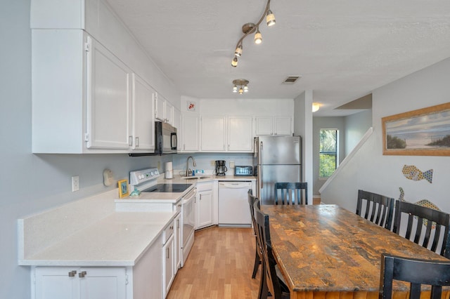 kitchen featuring white appliances, a sink, light wood finished floors, white cabinets, and a textured ceiling