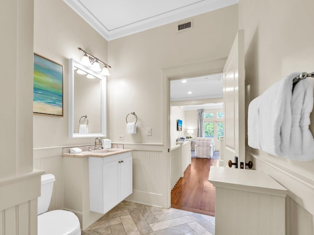 bathroom with ornamental molding, wainscoting, toilet, vanity, and a decorative wall