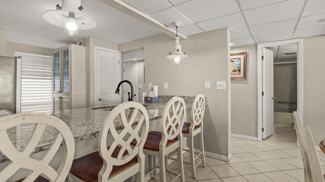 dining area featuring bar with sink, light tile patterned flooring, and baseboards