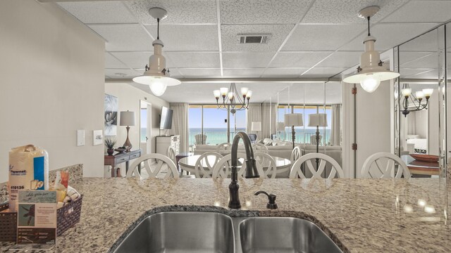 kitchen with a drop ceiling, a sink, stone countertops, a chandelier, and decorative light fixtures