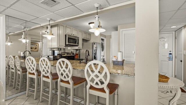 kitchen with appliances with stainless steel finishes, estacked washer and dryer, light tile patterned floors, a drop ceiling, and a peninsula