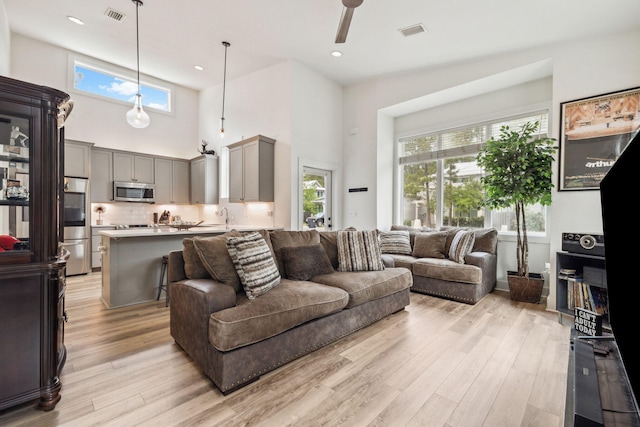 living room with light wood-style flooring, healthy amount of natural light, ceiling fan, a high ceiling, and recessed lighting