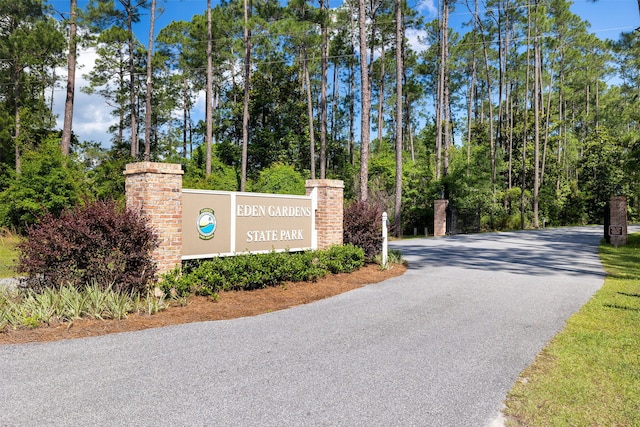 community / neighborhood sign with asphalt driveway and view of wooded area