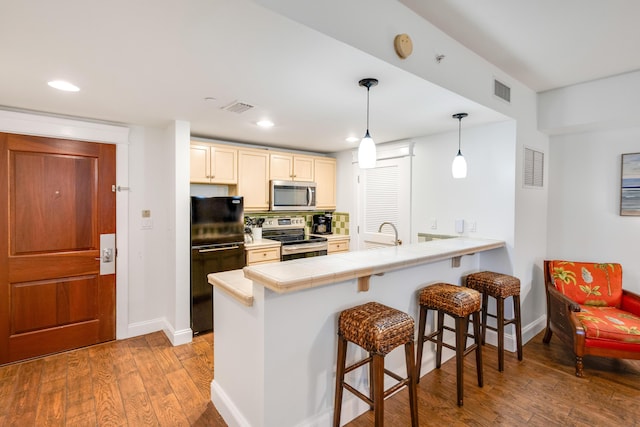 kitchen with appliances with stainless steel finishes, a kitchen breakfast bar, wood finished floors, a peninsula, and baseboards