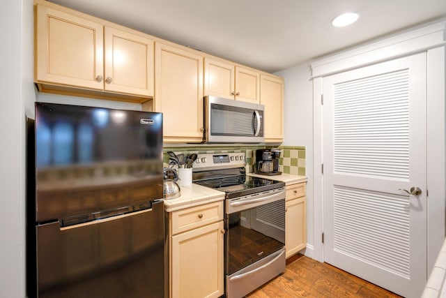 kitchen with stainless steel appliances, tile countertops, tasteful backsplash, light wood finished floors, and recessed lighting