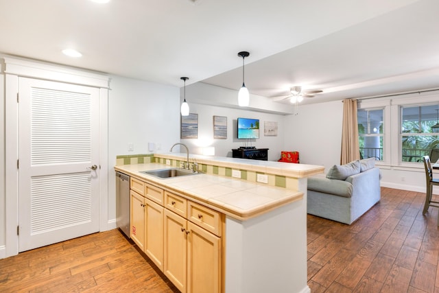 kitchen with a sink, a peninsula, dishwasher, tile countertops, and light wood-type flooring