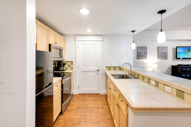 kitchen featuring stainless steel appliances, a sink, tile countertops, light wood-type flooring, and a peninsula