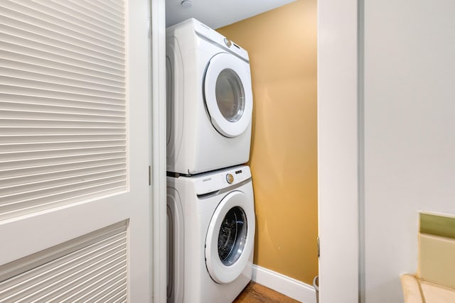 clothes washing area featuring stacked washer / drying machine, baseboards, and wood finished floors