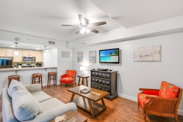 living area featuring wood finished floors, a ceiling fan, and baseboards