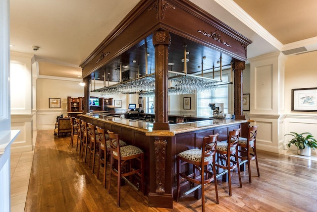 indoor dry bar with wood finished floors, a decorative wall, ornamental molding, and wainscoting