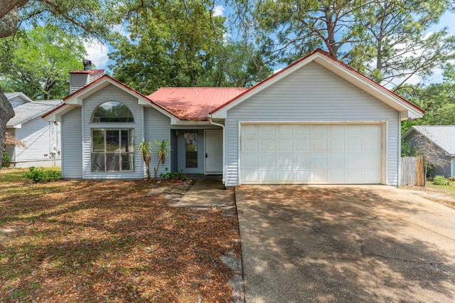 view of front of house with driveway, an attached garage, a chimney, metal roof, and fence