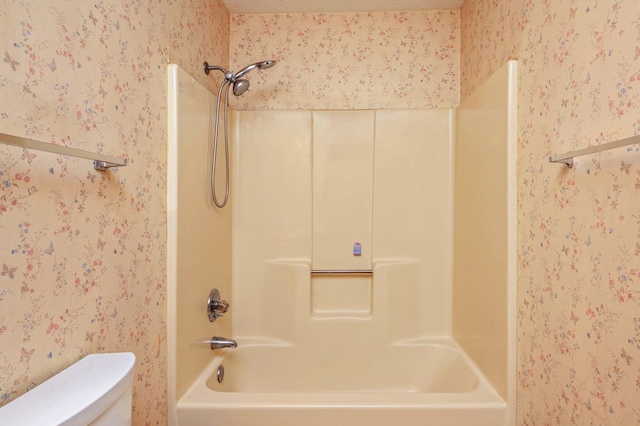 bathroom with wallpapered walls, toilet, shower / washtub combination, and a textured ceiling