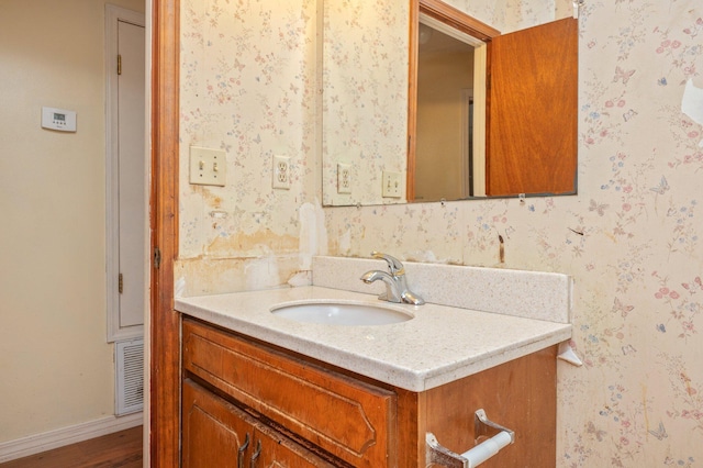 bathroom with vanity, wallpapered walls, wood finished floors, and baseboards