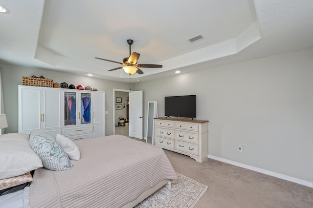 bedroom featuring a raised ceiling, light colored carpet, recessed lighting, baseboards, and a ceiling fan