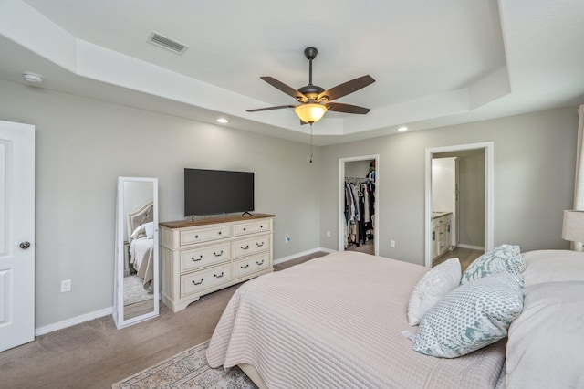 carpeted bedroom with a tray ceiling, a walk in closet, baseboards, a closet, and ensuite bathroom