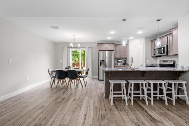 kitchen with stainless steel appliances, light wood finished floors, a kitchen bar, light stone counters, and recessed lighting