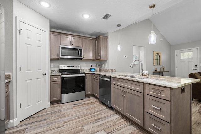 kitchen with appliances with stainless steel finishes, a sink, a peninsula, light wood-style floors, and lofted ceiling
