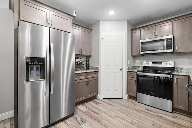 kitchen with stainless steel appliances, light wood-type flooring, light stone counters, baseboards, and recessed lighting