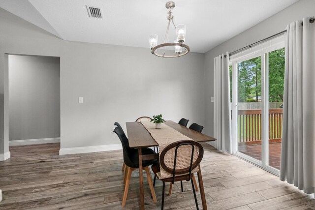 dining area featuring a chandelier, wood finished floors, baseboards, and vaulted ceiling
