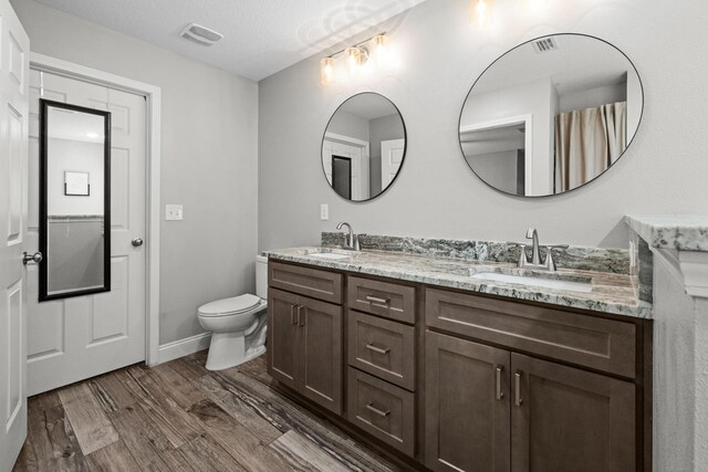 bathroom with wood finished floors, toilet, and double vanity