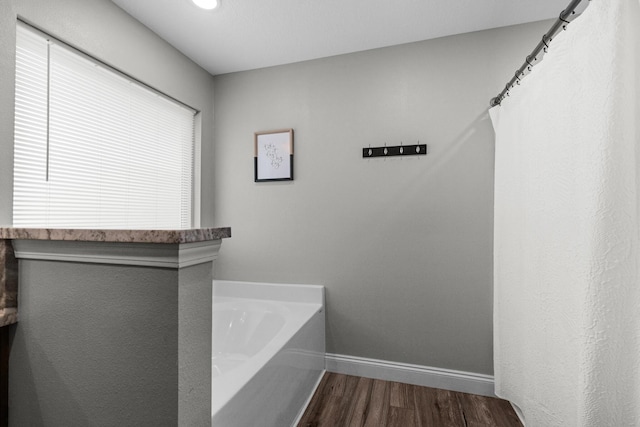 full bathroom featuring a bath, baseboards, and wood finished floors