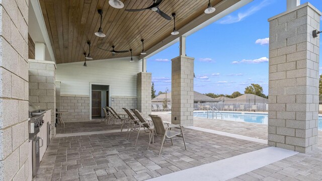 view of patio featuring ceiling fan, a community pool, an outdoor kitchen, and fence