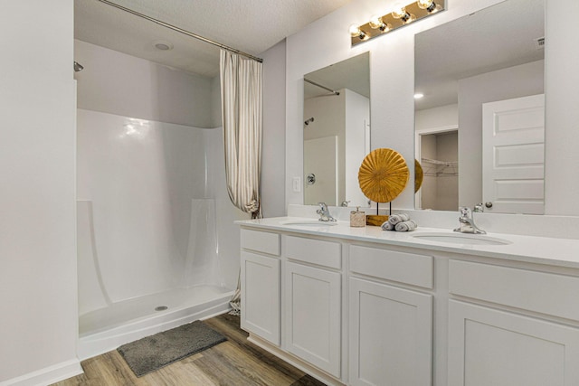 bathroom featuring wood finished floors, a shower with shower curtain, double vanity, and a textured ceiling