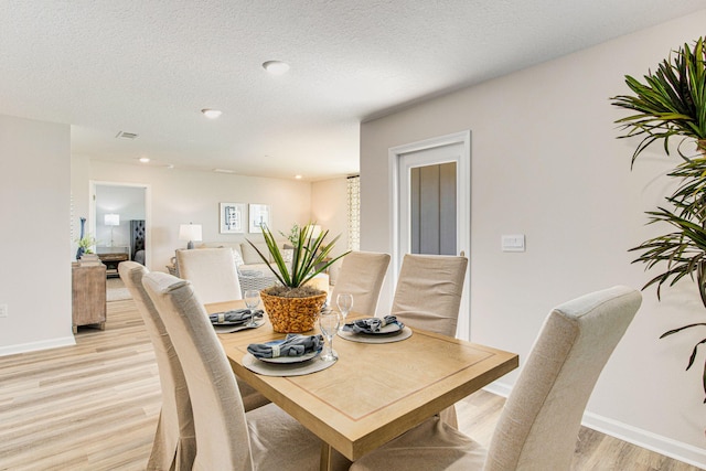 dining area with light wood finished floors, baseboards, a textured ceiling, and recessed lighting