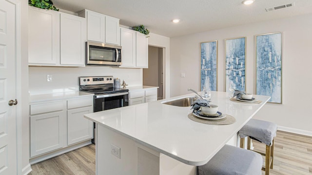 kitchen featuring appliances with stainless steel finishes, a sink, light wood finished floors, light countertops, and white cabinetry