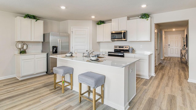 kitchen featuring appliances with stainless steel finishes, light wood-type flooring, a kitchen bar, white cabinetry, and recessed lighting