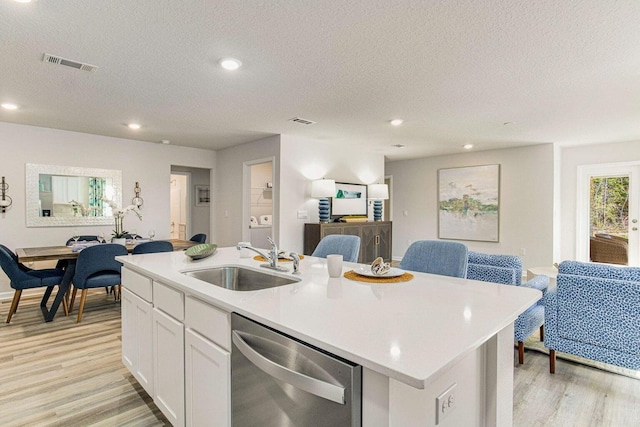 kitchen with stainless steel dishwasher, a sink, open floor plan, light wood-style floors, and a textured ceiling